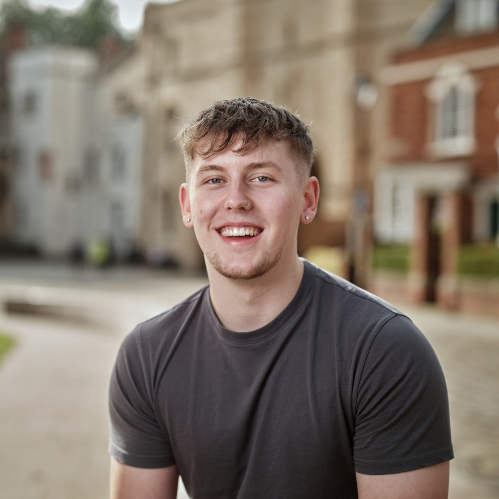 A student wearing a grey t shirt smiling at the camera