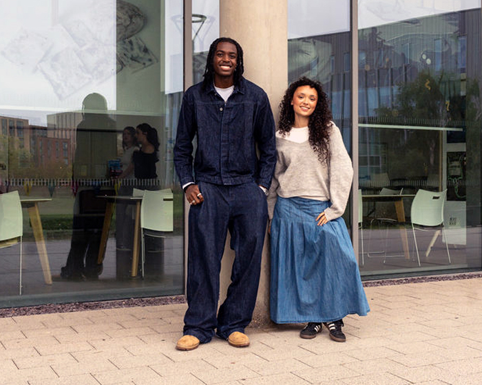 Two students leaning up a pillar outside a glass building
