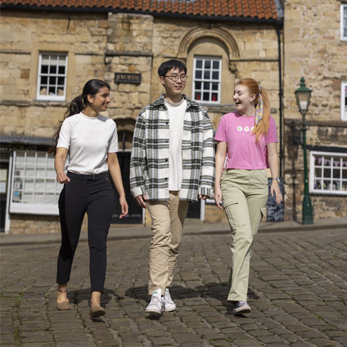 Three students walking along a cobbled street